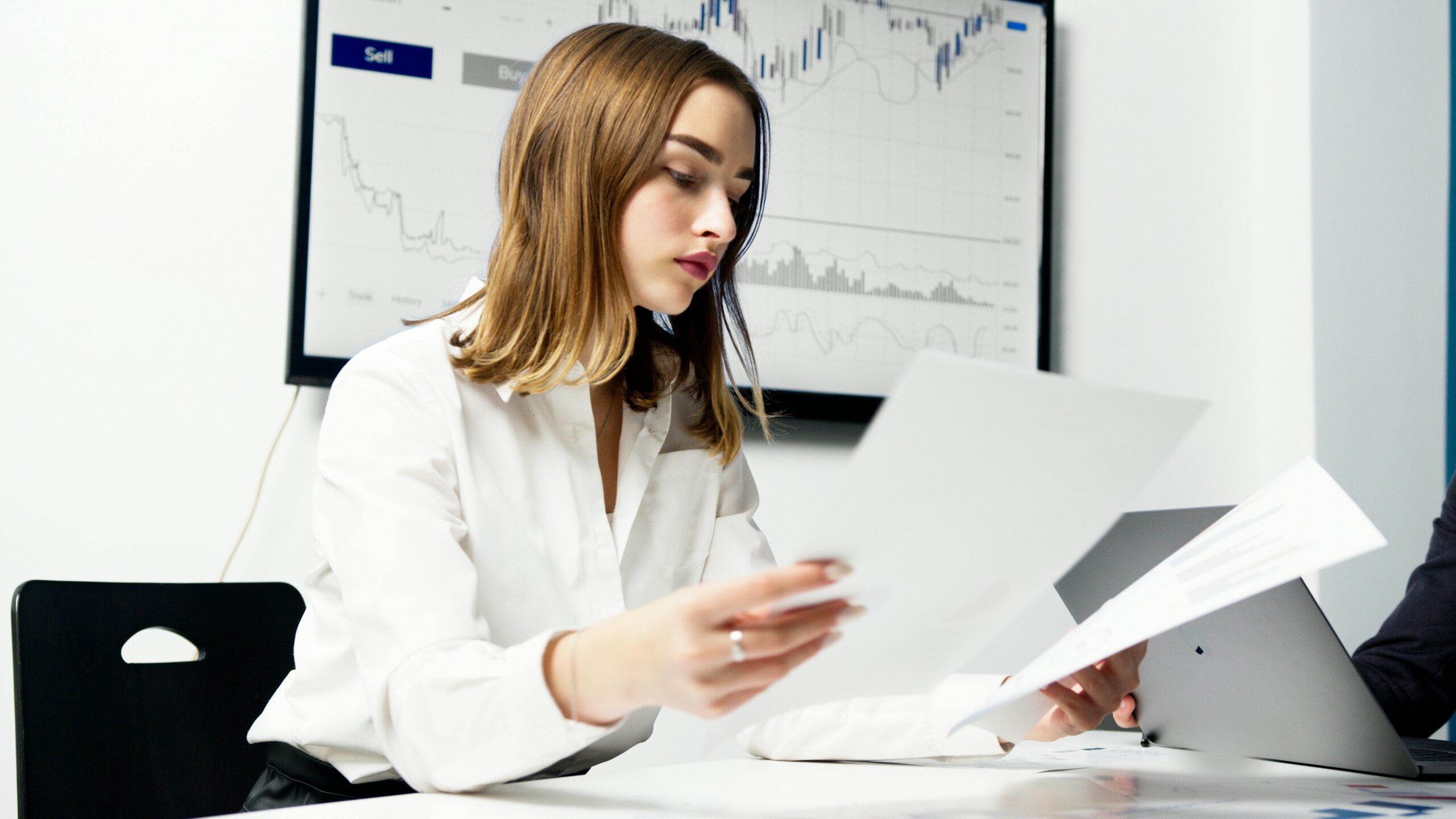 Focused woman analyzing financial reports in a modern office setting with charts and graphs.