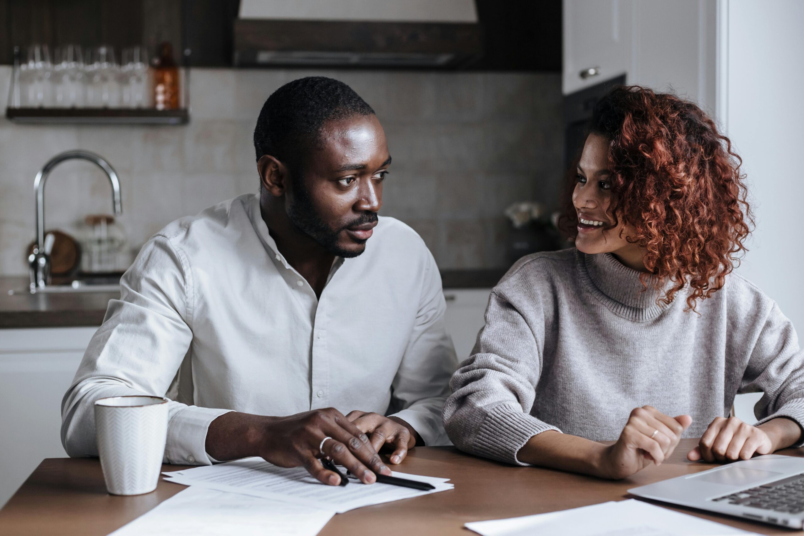 Black couple collaborating on a project at their kitchen table, showcasing teamwork and home office lifestyle.